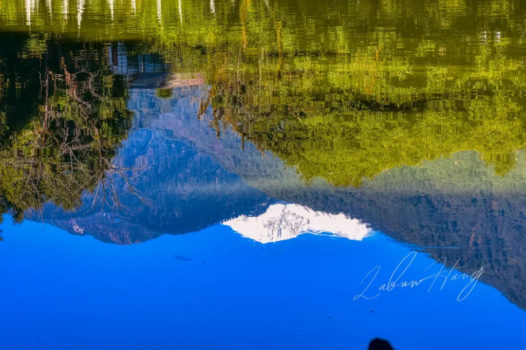 Kathok Lake in Yuksom, West Sikkim, showing perfect mirror reflection of snow-capped Kabru mountain peak surrounded by lush green forest and blue sky