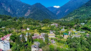 Aerial view of Yuksom village in West Sikkim with traditional houses nestled among lush green hills and Mount Kabru peaks in the background