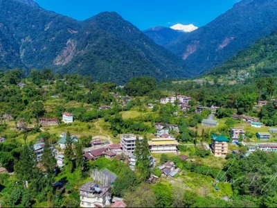 Aerial view of Yuksom village in West Sikkim with traditional houses nestled among lush green hills and Mount Kabru peaks in the background