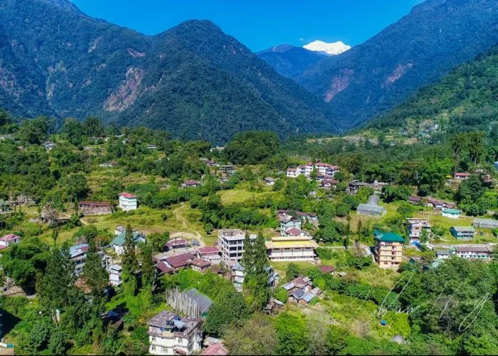 Aerial view of Yuksom village in West Sikkim with traditional houses nestled among lush green hills and Mount Kabru peaks in the background