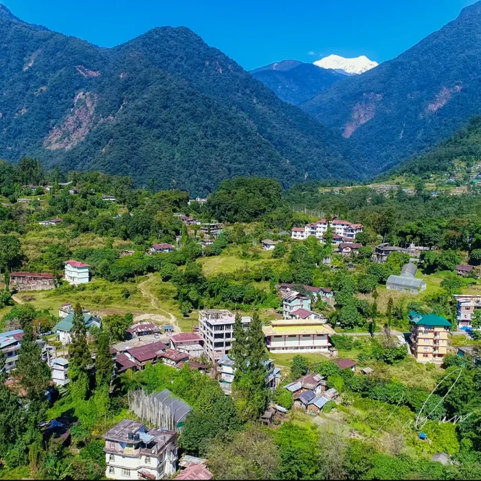 Aerial view of Yuksom village in West Sikkim with traditional houses nestled among lush green hills and Mount Kabru peaks in the background